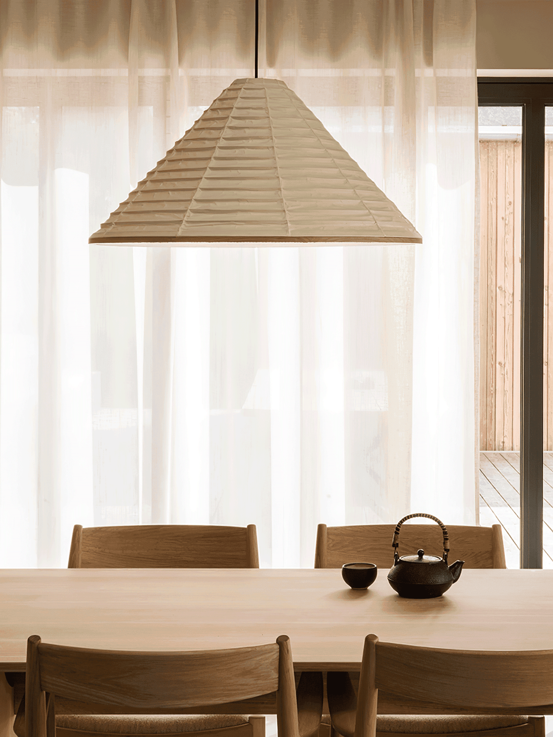 Large Washi paper pendant lamp above a minimalist wood dining table with a traditional black teapot
