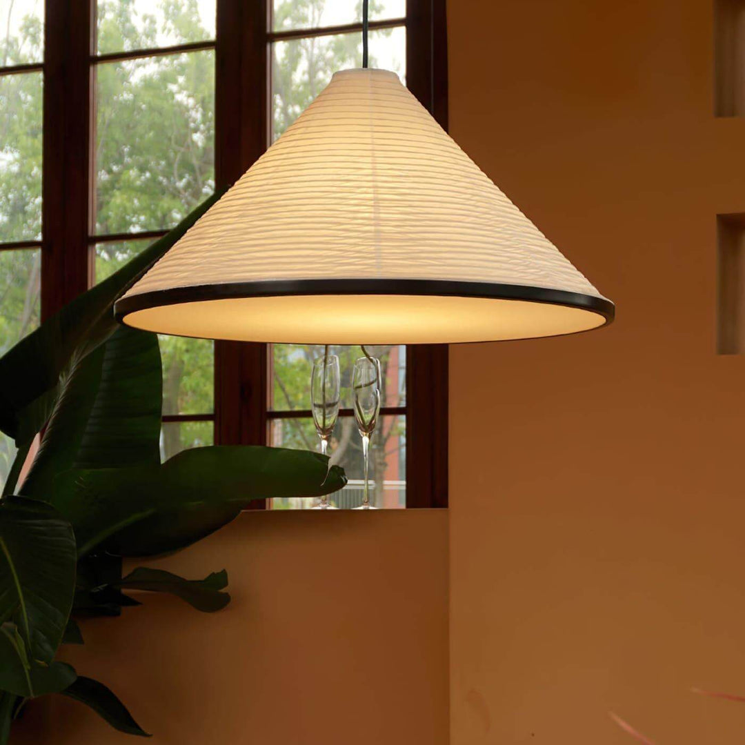 Close view of the illuminated Washi Paper Hat Pendant Lamp beside a window and tropical green plant