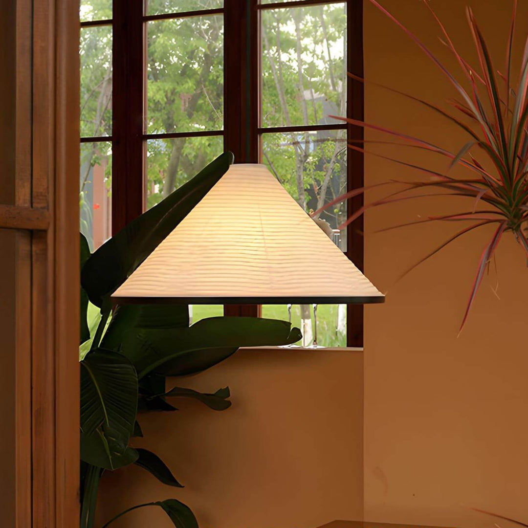 Front view of the Washi paper cone pendant light hanging against warm walls and leafy indoor plants