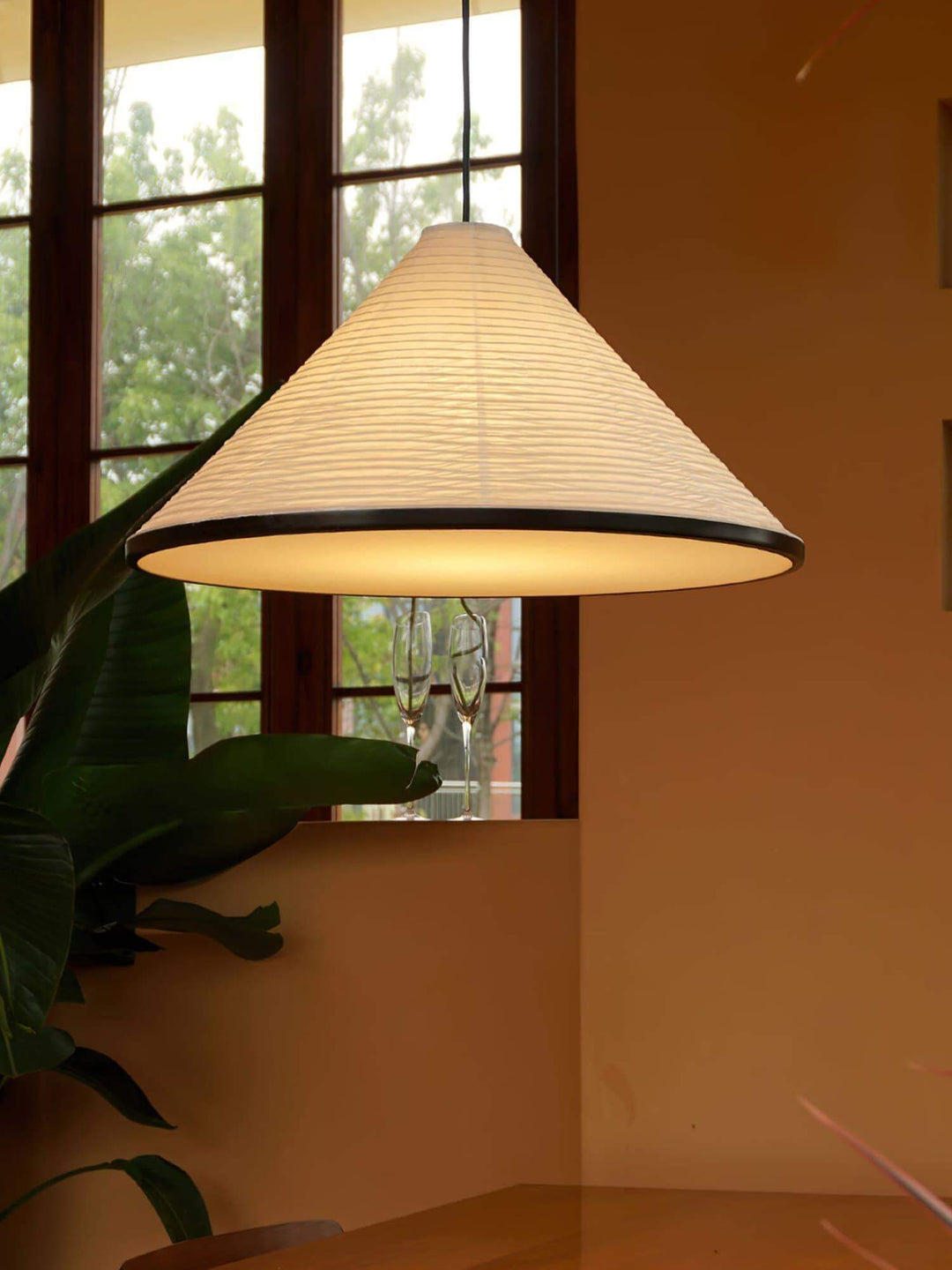 Close view of the illuminated Washi paper pendant lamp with black trim beside a window and green plant