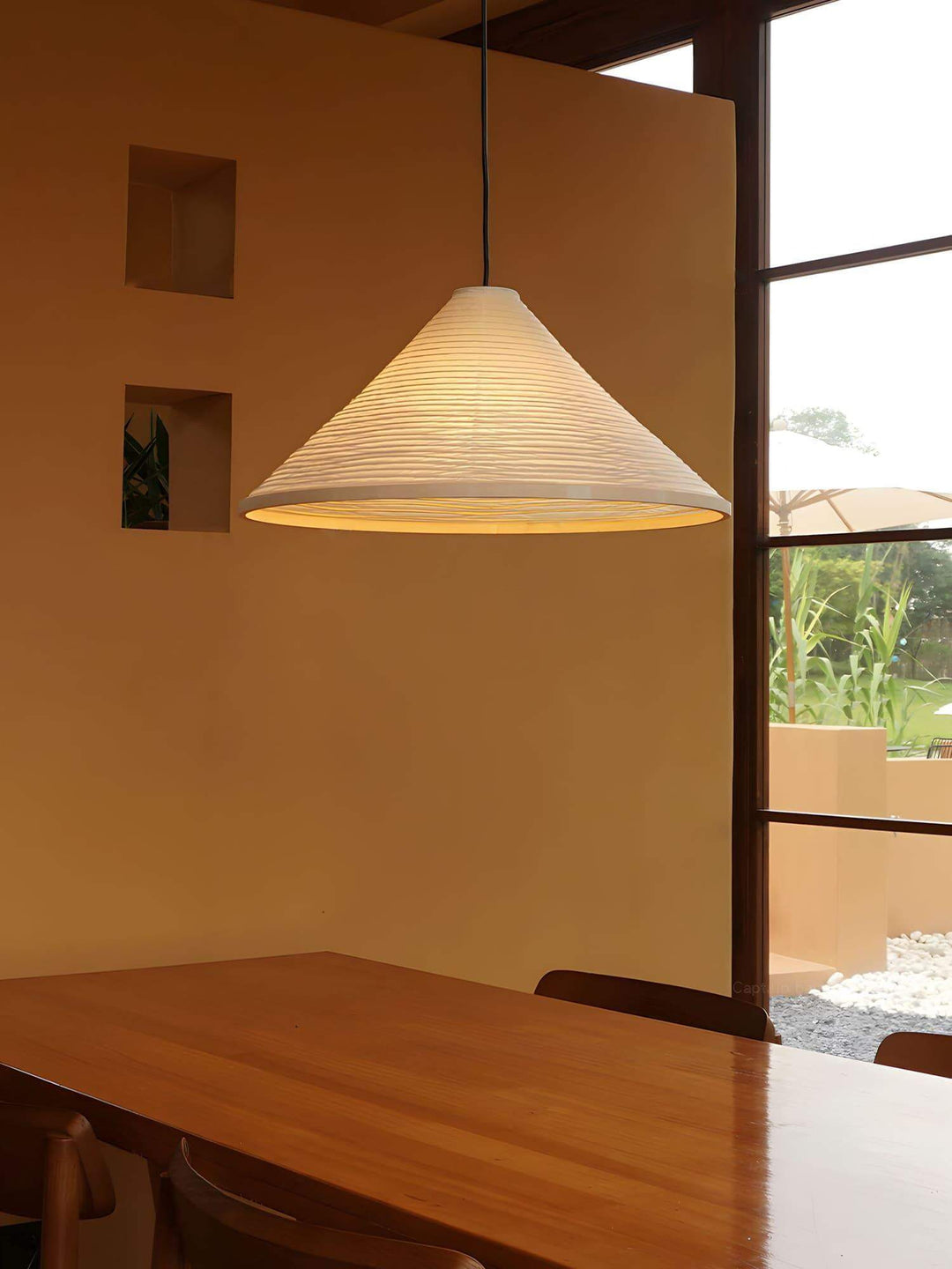 Washi paper pendant lamp casting warm light above a long wood dining table beside tall windows