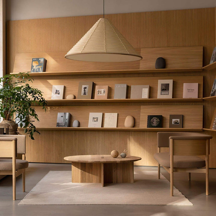 Washi paper cone pendant light above a round coffee table in a warm wood library lounge