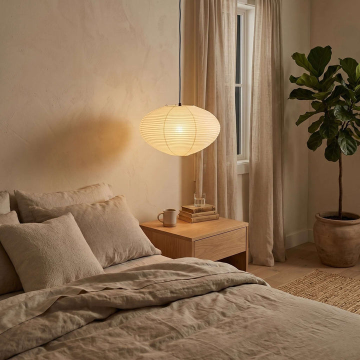 Washi paper pendant light beside a bed in a warm neutral bedroom.
