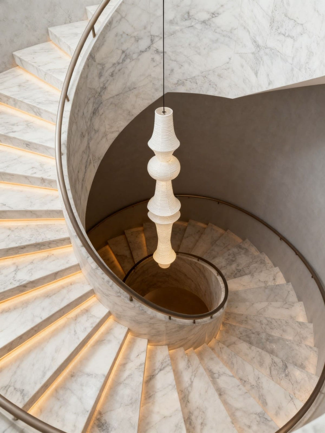 Washi paper pendant light hanging through the center of a curved marble staircase viewed from above