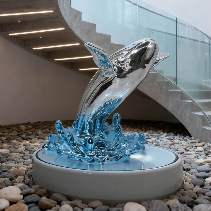 Silver and blue whale sculpture on a round pedestal beneath a curved concrete staircase.