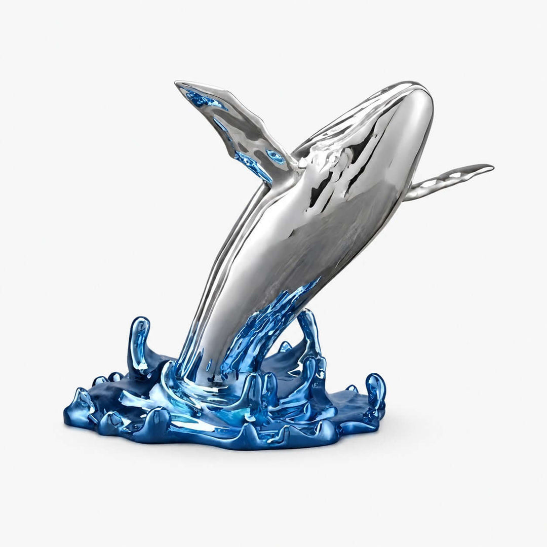 Silver chrome-plated resin whale sculpture leaping from a glossy blue wave base on a white background.
