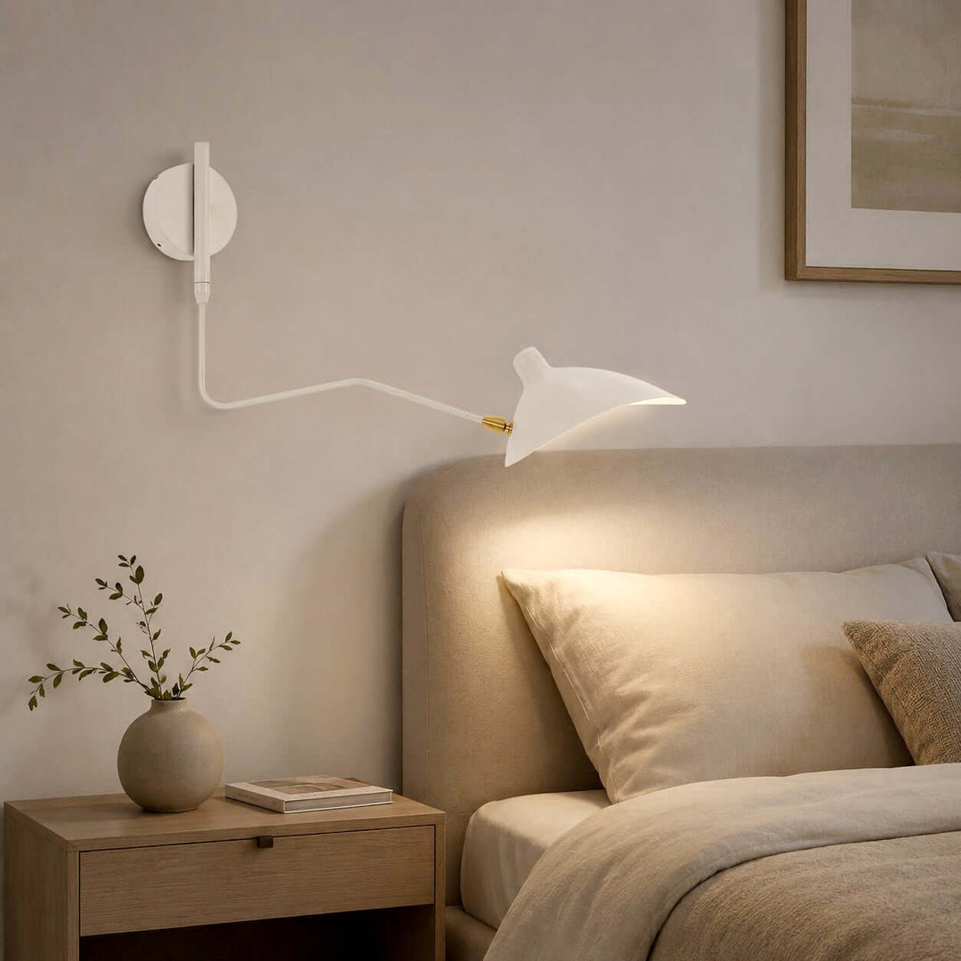 White adjustable bedside wall sconce casting warm light over an upholstered bed