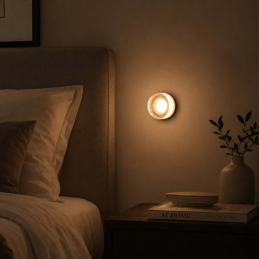 White Dimple wall sconce glowing beside a bed in a dark bedroom.