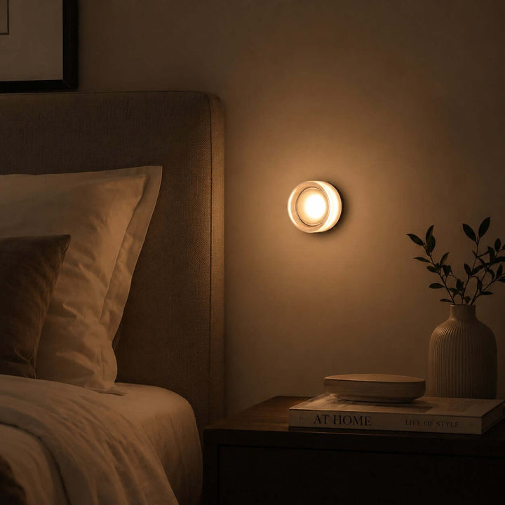 White Dimple wall sconce glowing beside a bed in a dark bedroom.