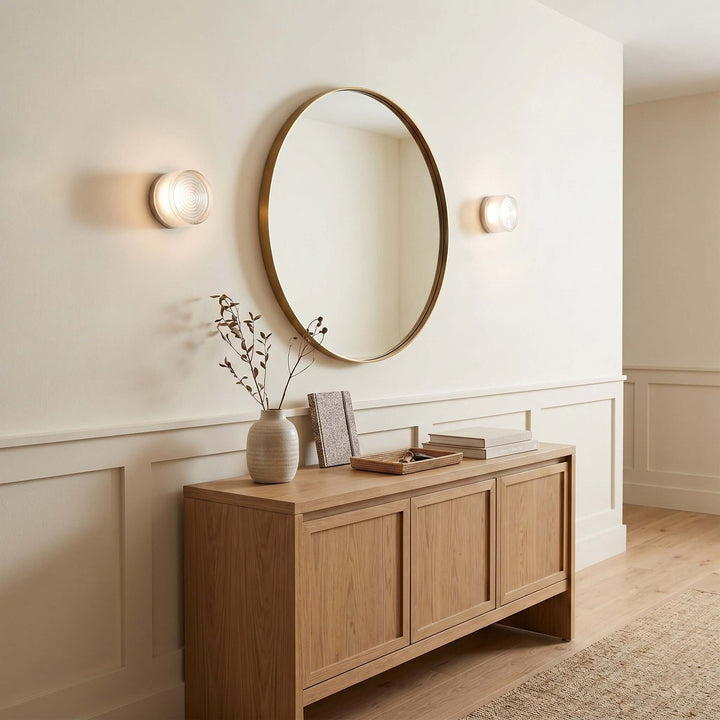White Dimple wall sconces beside a round mirror above a wood console.