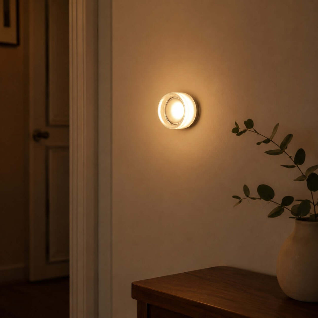 White Dimple wall sconce glowing softly above a wood table.
