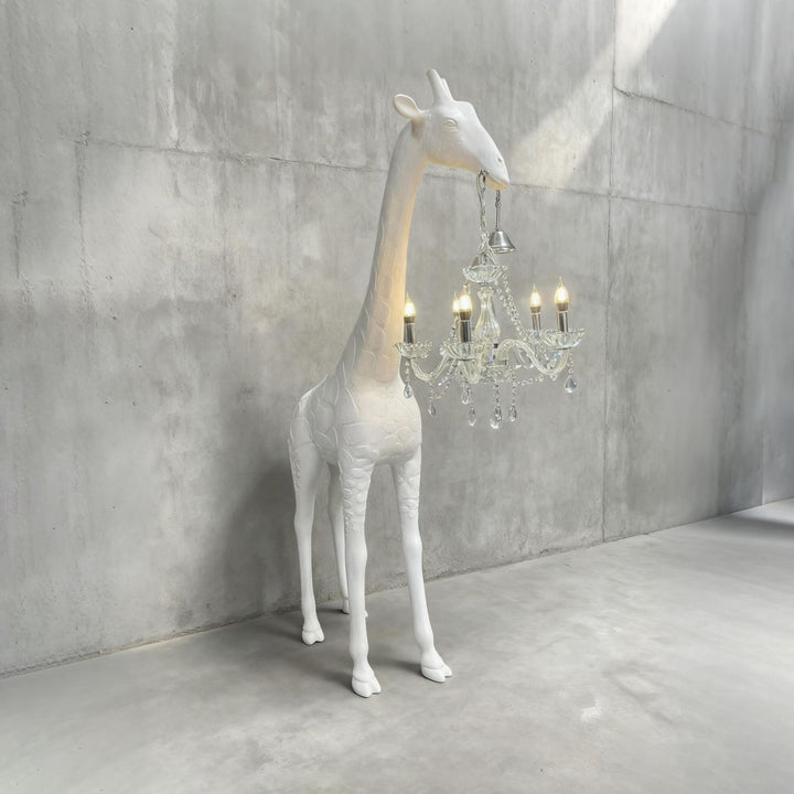 White and silver giraffe floor lamp with a crystal chandelier against a concrete wall