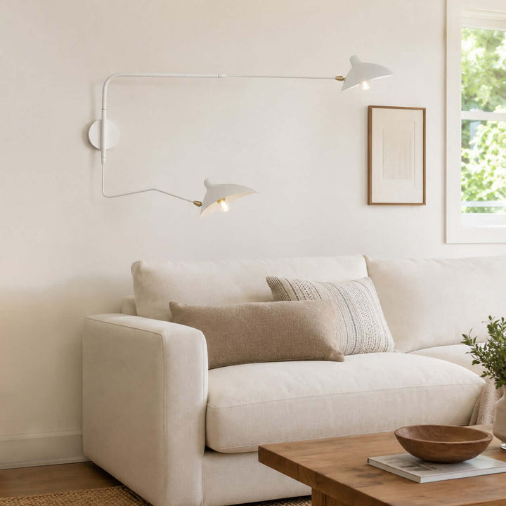 White two-light swing arm wall sconce with brass joints above a cream sofa