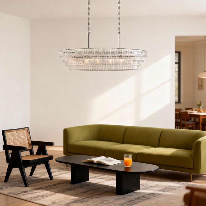 Linear clear glass chandelier hanging over a green sofa and black coffee table