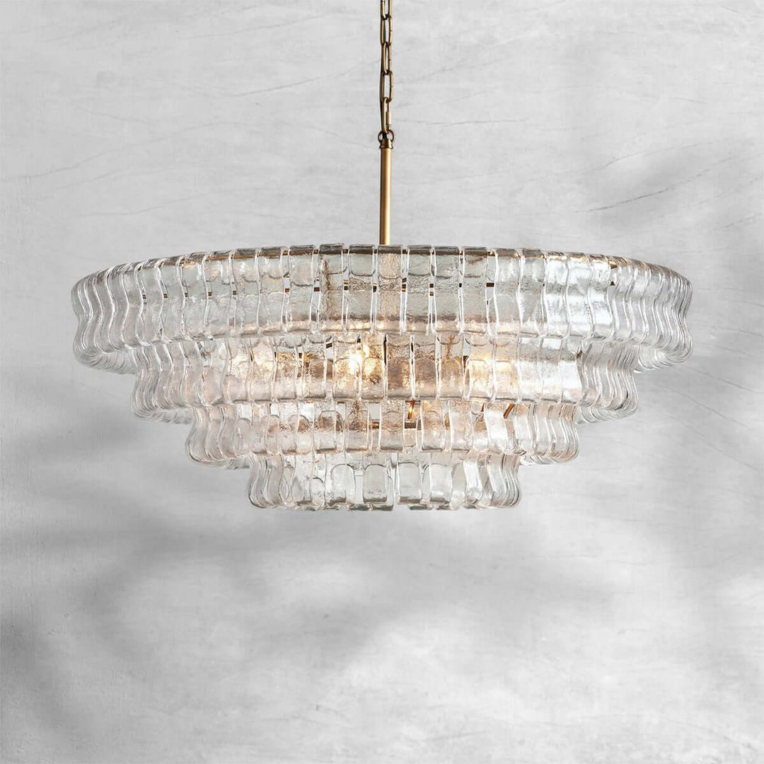 Clear round glass chandelier with a gold center stem and warm bulbs on a gray background