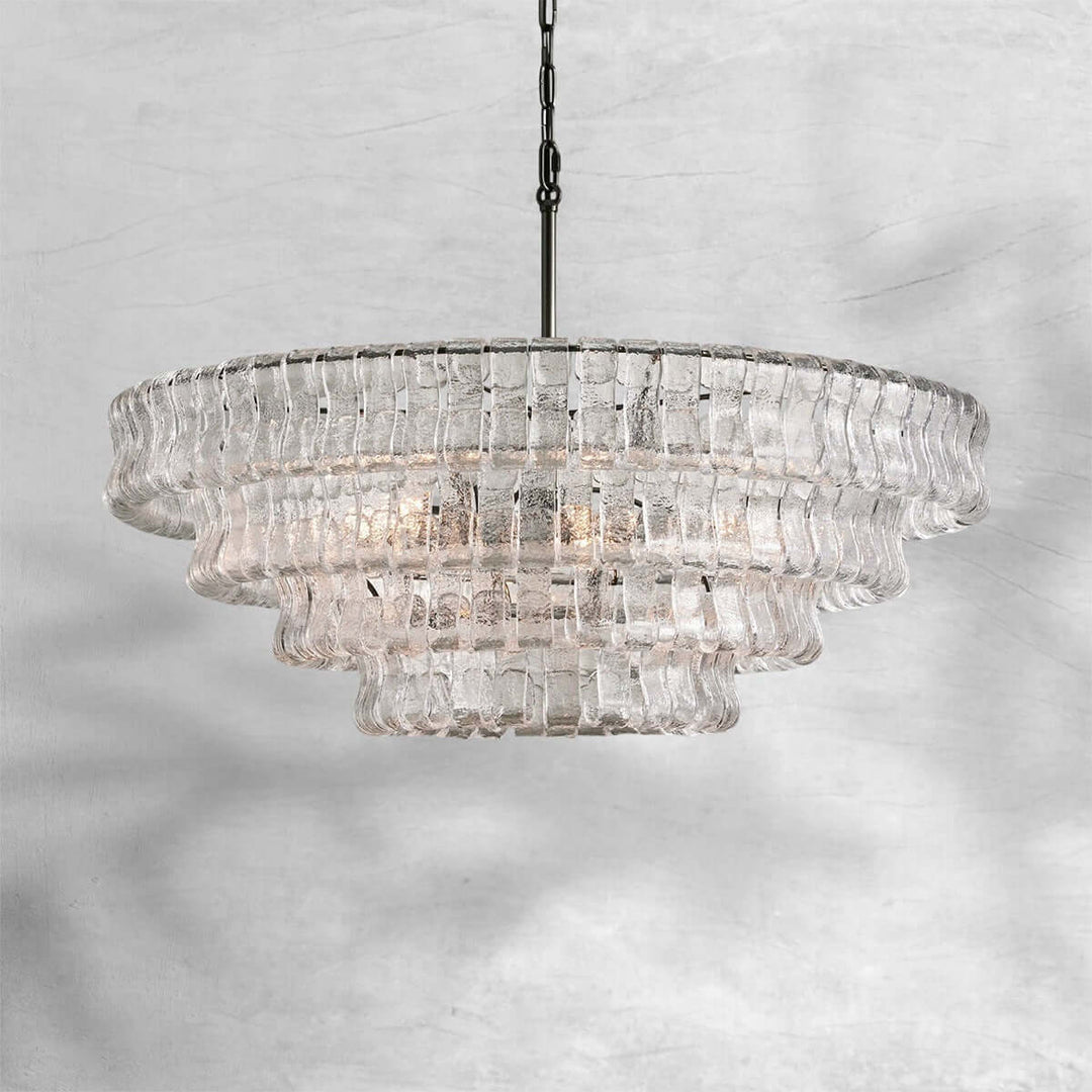 Clear round glass chandelier with a black chain and warm bulbs on a gray background