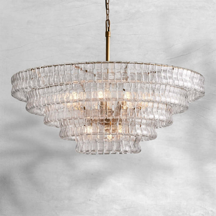 Wide clear glass chandelier with a gold stem and warm bulbs on a gray background