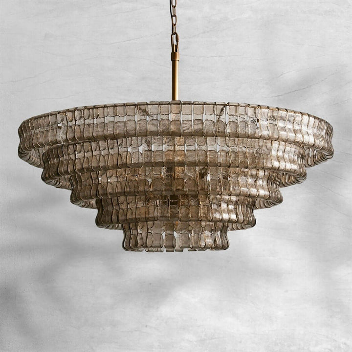 Smoky wide glass chandelier with a gold stem and layered shade on a gray background