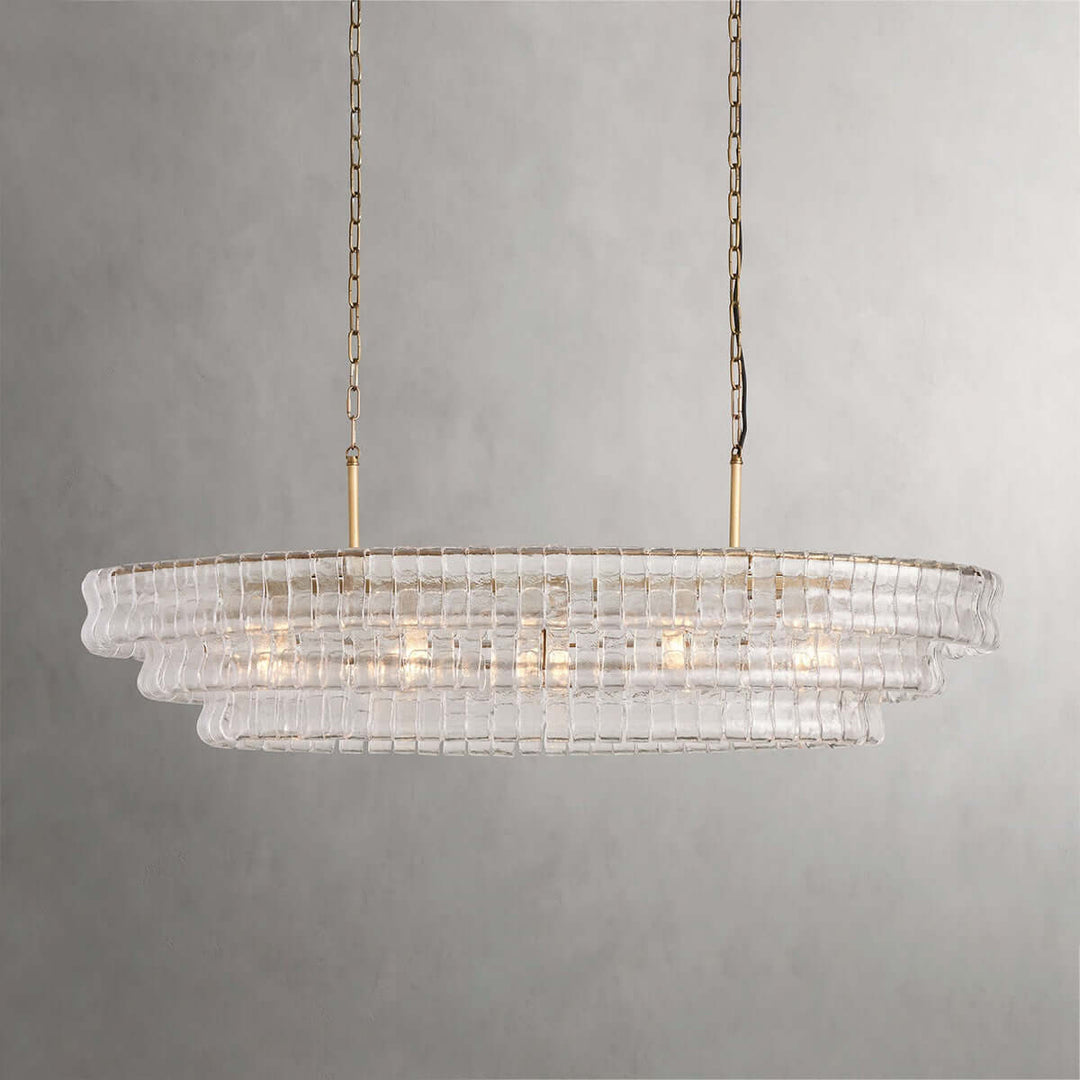 Linear clear glass chandelier with two gold chains and warm bulbs on a gray background