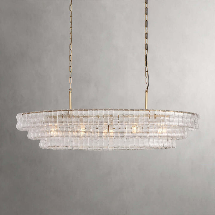 Linear clear glass chandelier with two gold chains and warm bulbs on a gray background