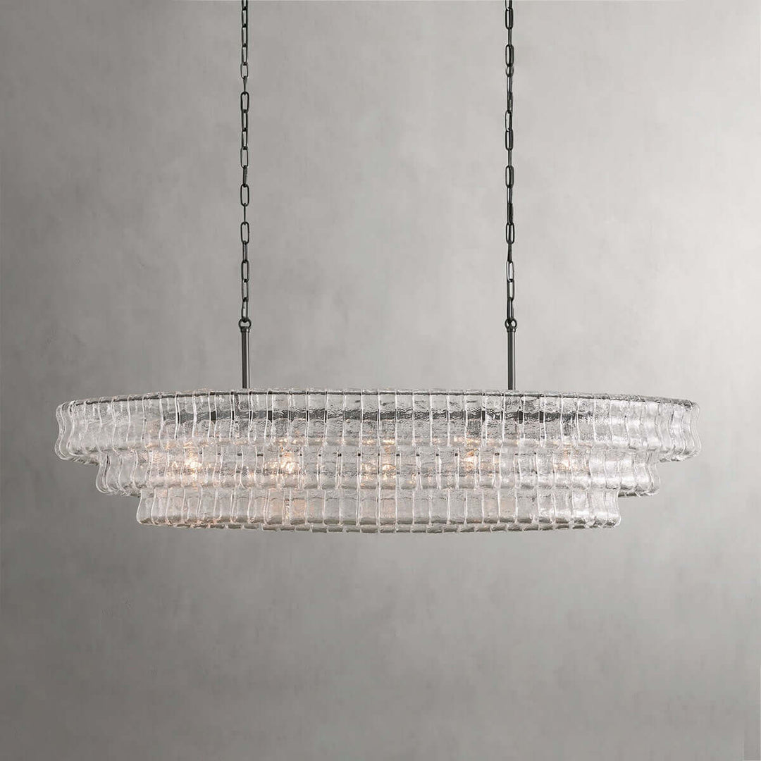 Linear clear glass chandelier with two black chains and warm bulbs on a gray background