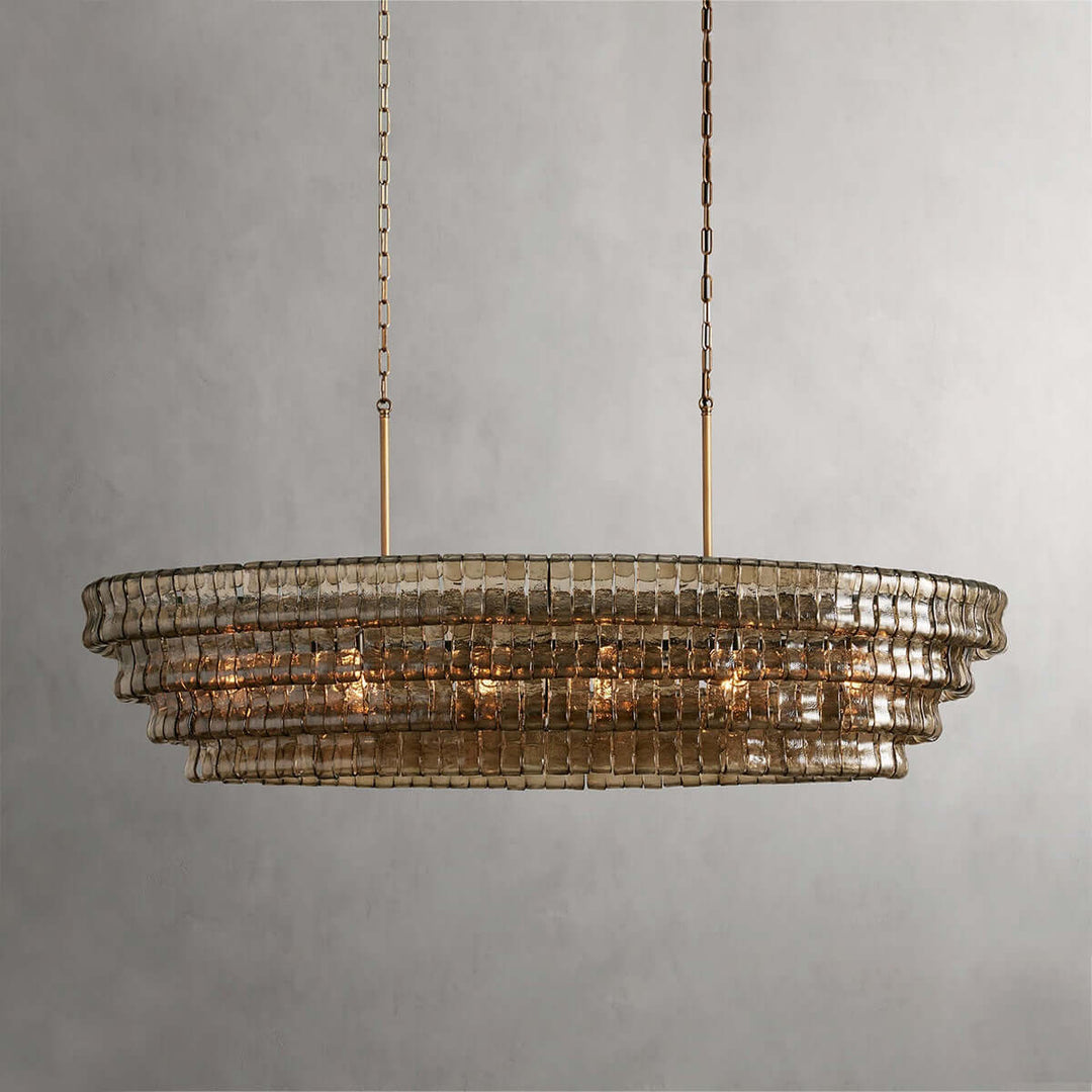 Close front view of a linear smoky glass chandelier with gold chains and warm bulbs