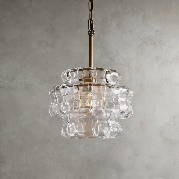 Small clear glass chandelier with a gold stem and wavy shade against a gray wall