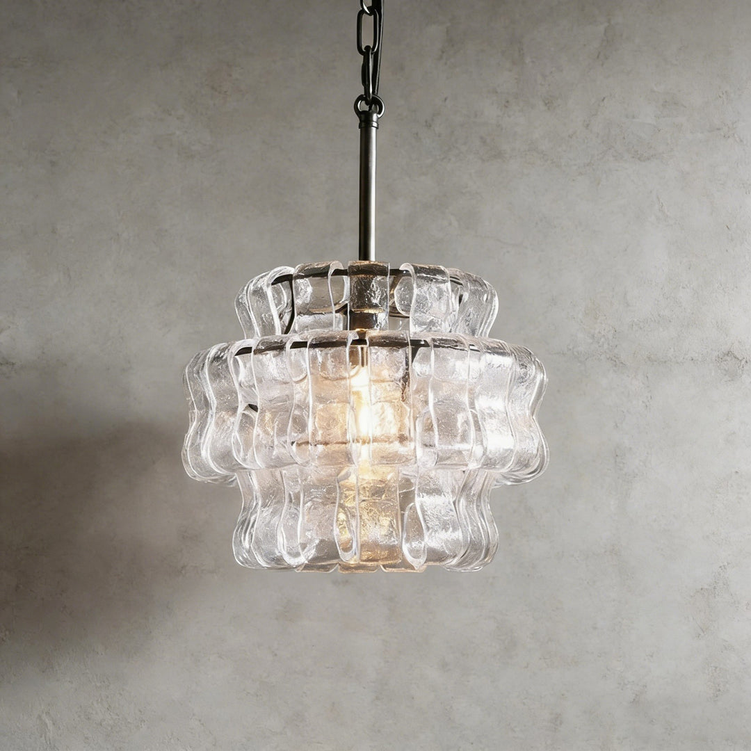 Small clear glass chandelier with a black stem and warm glowing bulb against a gray wall