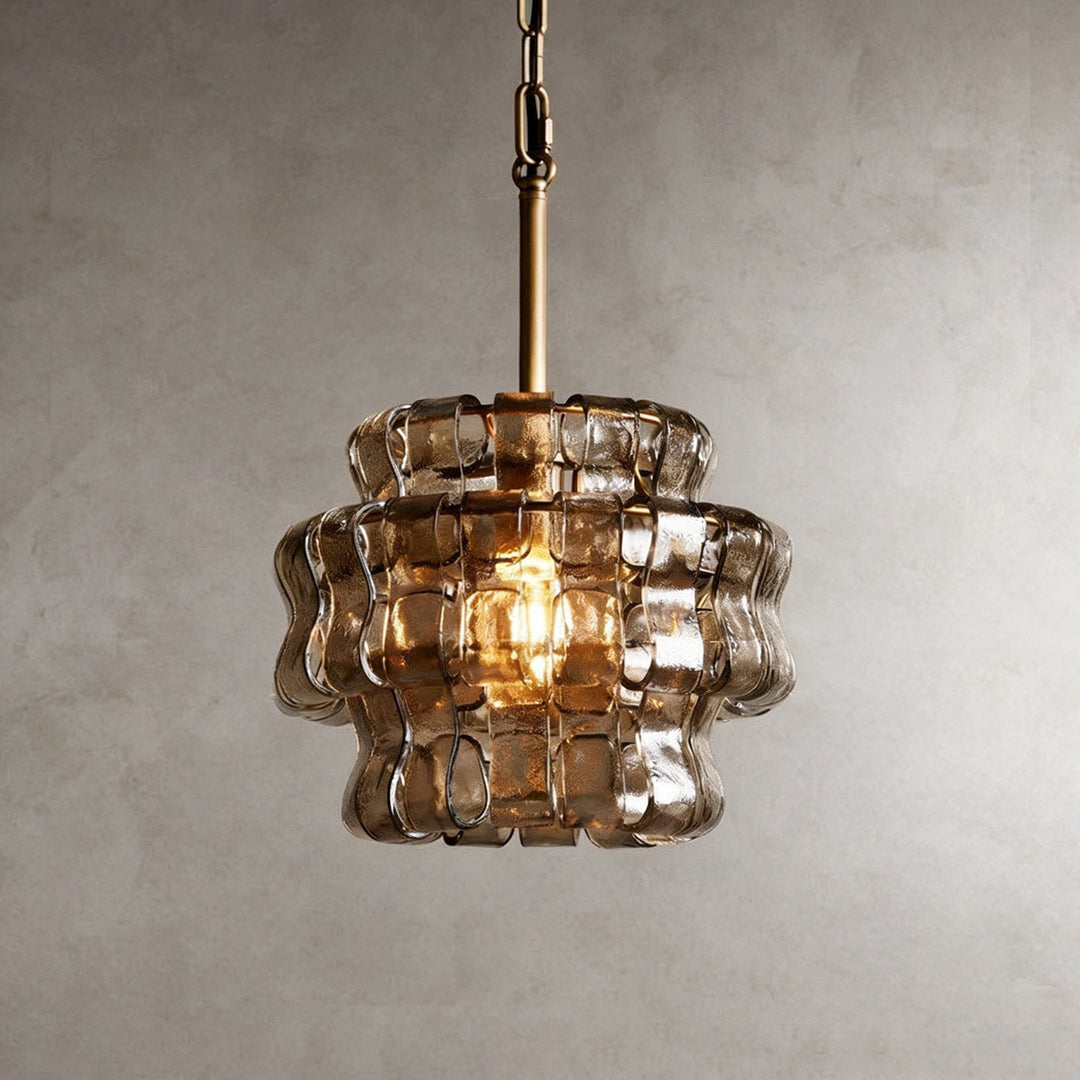 Small smoky glass chandelier with a gold stem and warm glowing bulb against a gray wall