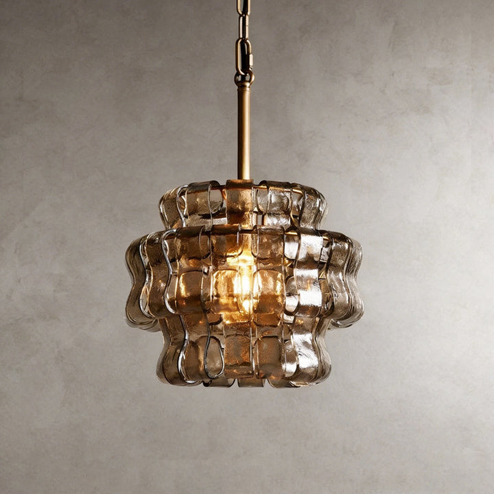 Small smoky glass chandelier with a gold stem and warm glowing bulb against a gray wall