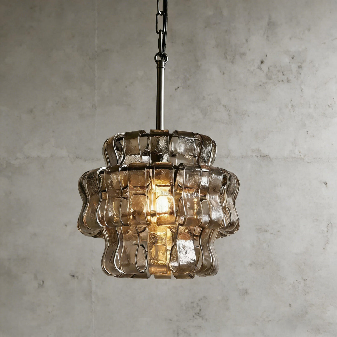 Small smoky glass chandelier with a black stem and warm glowing bulb against a gray wall